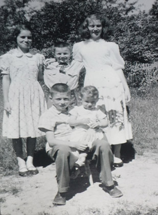 A picture of the five of us outside at the Quinn house.  I’m thinking this was taken on a Sunday, judging by the fact that I’m wearing my Sunday tie.  I’ve got my arms around my big sisters Marjorie and Katharine.  Johnny is sitting on a little stool with Leonard on his knees.