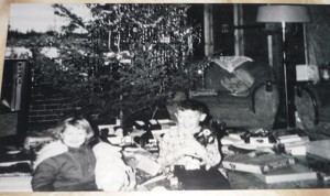 A picture of Leslie and Leonard with their Christmas presents that winter (December 1961), which shows that the house that Dad built was still unfinished. Note the bare two-by-four studs on the living room walls. That’s just decorative brick fireplace paper taped on the wall behind the Christmas tree.