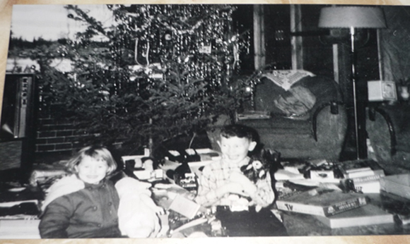 A picture of Leslie and Leonard with their Christmas presents that winter (December 1961), which shows that the house that Dad built was still unfinished.  Note the bare two-by-four studs on the living room walls.  That’s just decorative brick fireplace paper taped on the wall behind the Christmas tree.  